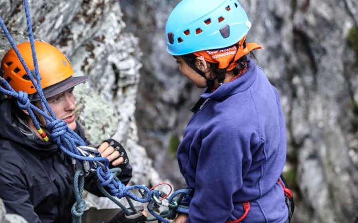 an instructor gives direction to a student preparing to rock climb on an outward bound trip in north carolina